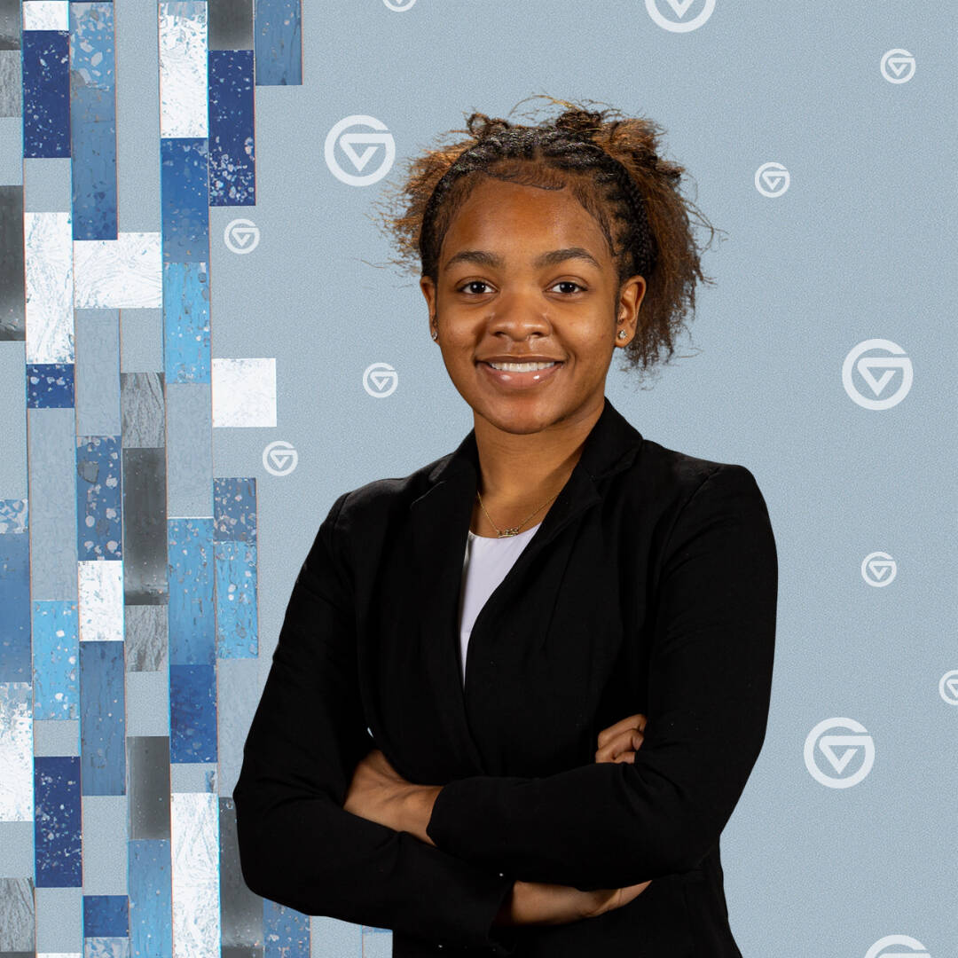 African American woman in a black suit with a gray, and blue tiled background